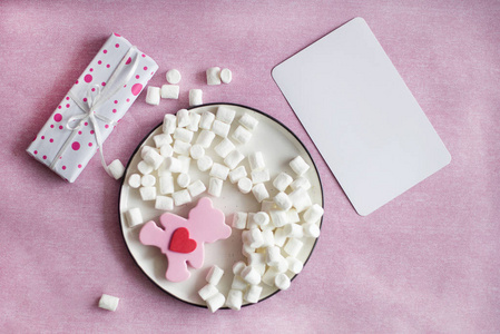 用丝带系的礼品盒位于粉红色背景盒上，粉红色熊玩具棉花糖与白色卡片复制空间水平
