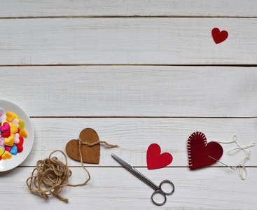 情人节2月14日的概念。 用剪刀和红白装饰毡制作情人节礼物的过程，一颗心在白色复古的木制背景上未完成。 文本空间