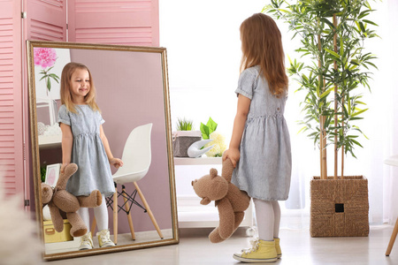 可爱的小女孩带着泰迪熊照镜子在家里