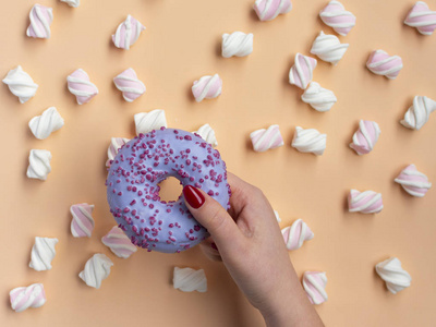 s hand holding donut with marshmallow on peach background