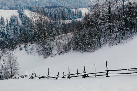 覆盖着雪帽的木栅栏。 冬季乡村景观村或农场白雪覆盖的山脉和森林背景