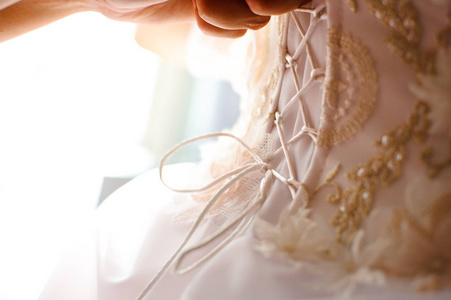 s hands tie a ribbon on the corset of a wedding dress.