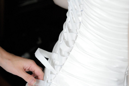 s hands tie a ribbon on the corset of a wedding dress.