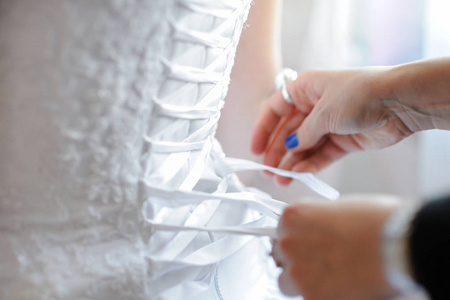 s hands tie a ribbon on the corset of a wedding dress.