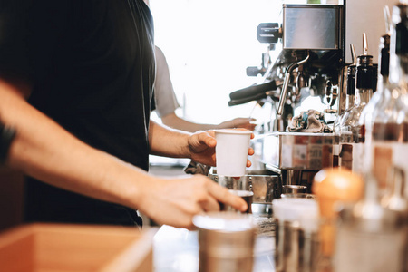 一个年轻的时尚男人, 穿着休闲装, 在现代化的咖啡店煮咖啡。显示了手和杯子