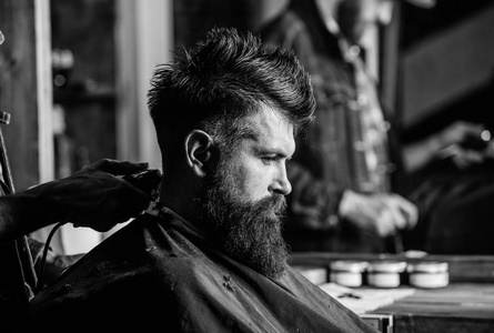 理发师的手, 头发剪, 关闭。时髦的大胡子客户得到的发型。理发店概念。有胡子的男人在美发椅, 沙龙背景。理发师工作与理发剪