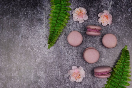 法国通心粉饼干甜点粉红色紫丁香，深色背景，粉红色花朵和绿叶。