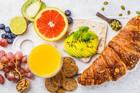 健康素食早餐，牛角面包，鳄梨吐司，水果和果汁放在白色盘子里，俯视图。