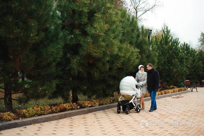 一家人带着婴儿车在秋季公园散步.妈妈 爸爸和婴儿