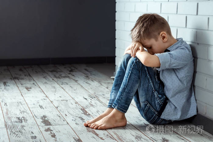 一个小男孩独自坐在墙附近的学校里,有一种悲伤的感觉