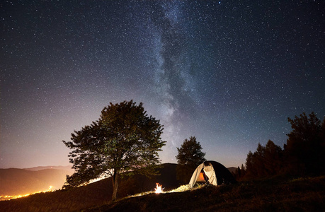 在充满星星和银河的神奇夜空下照亮帐篷和篝火