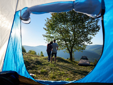阳光明媚的早晨，两个快乐的年轻男女徒步旅行者在露营和大树附近休息