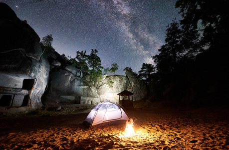 白色发光的旅游帐篷和篝火在惊人的夜空下充满星星和银河