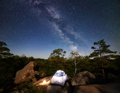 在充满星星和银河的神奇夜空下，白色旅游帐篷和篝火