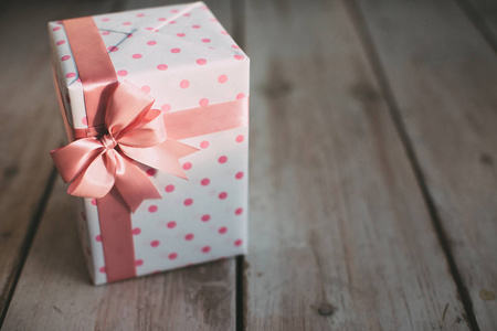 时尚的手工礼物。 带有圆点的礼品盒，木制背景上有粉红色的蝴蝶结。