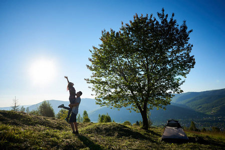 在阳光明媚的早晨，两个快乐的年轻人和女人徒步露营和大树附近休息