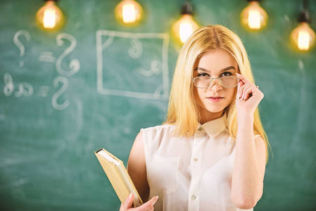 学生, 老师看起来自信的眼镜, 站在教室, 黑板上的背景, 弥散。有吸引力的讲师概念。有书的女人准备上课, 凝视观众