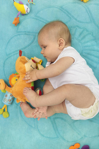 一个刚出生的小男孩躺在蓝色的毯子上，玩玩具，心情很有趣。