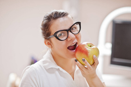 女牙医的肖像站在她的牙科办公室吃苹果。