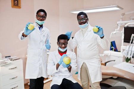 健康的牙齿是幸福的关键 三名非裔美国男医生在牙科诊所的同事手里拿着一个苹果。