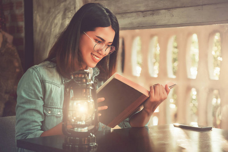 年轻漂亮的学生女孩在咖啡厅里读一本书，老式的色调
