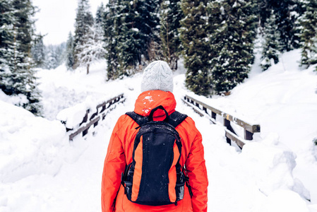 冬天的女人穿暖和的夹克和灰色的羊毛帽，背包在雪山上行走