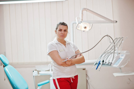 女牙医女士的肖像交叉手臂站在她的牙科办公室附近的椅子。