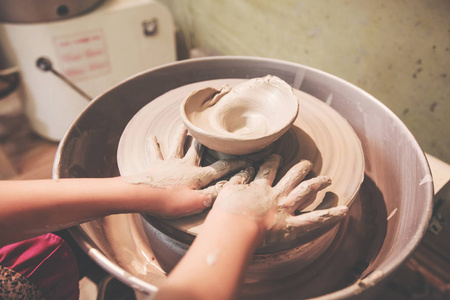 儿童手在车间陶轮上塑造粘土。