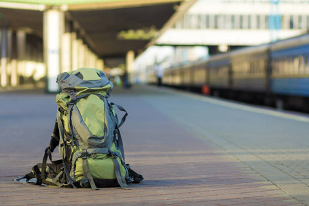 在模糊的背景下，在火车站平台上关闭大的绿色旅游背包。 旅游冒险和娱乐概念。