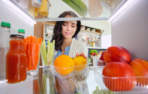 女性站附近打开冰箱充分的健康食品，蔬菜和水果的画像。女性肖像