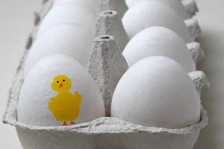 纸板箱的白色鸡蛋，一个鸡蛋，上面画着一只黄色的复活节鸡。
