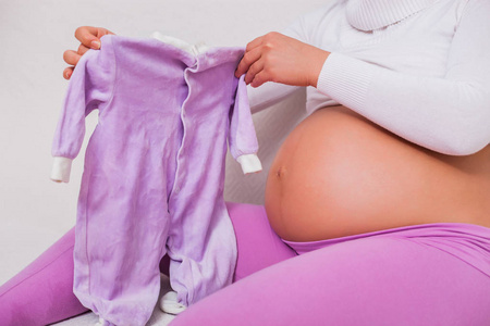 孕妇拿着婴儿的衣服。