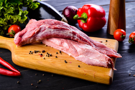 生猪肉。 新鲜牛排在木切割板上的深色背景。 生肋排配蔬菜和香料牛油