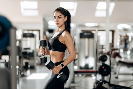 运动女孩穿着黑色的运动上衣和紧身衣建立肌肉与哑铃在健身房