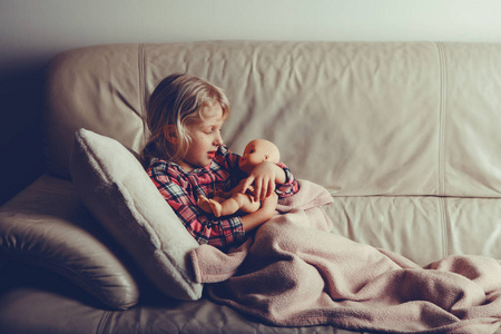 孩子玩玩具。 可爱的高加索女孩抱着娃娃。 孩子晚上躺在床上，晚上晚上躺在室内。 与胶片过滤器风格色调。 快乐的童年生活方式。