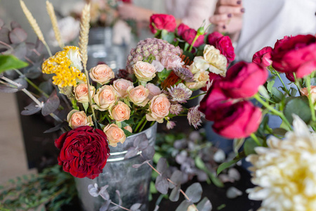 金属桶里的特写花。花店工作场所。妇女安排与玫瑰, 菊花, 康乃馨和其他花花束。大师班或课程中的花卉教师