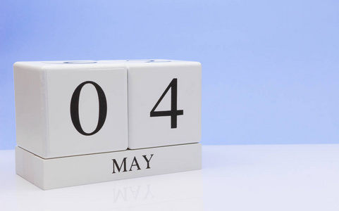 五月四日。 月4日每日日历在白色桌子上，反射浅蓝色背景。 春天的时间，空的文字空间