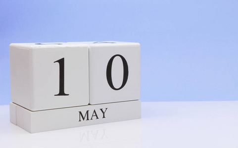 五月十日。 每月10日的每日日历在白色的桌子上，反射浅蓝色背景。 春天的时间，空的文字空间