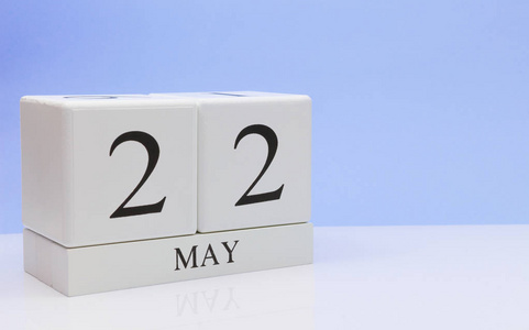 五月二十二日。 月22日每日日历在白色桌子上，反射浅蓝色背景。 春天的时间，空的文字空间