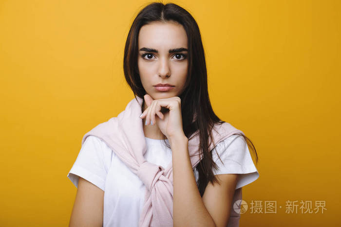 漂亮的欧洲女孩认真地看着镜头同时支撑着她的下巴在黄色背景前的拳头