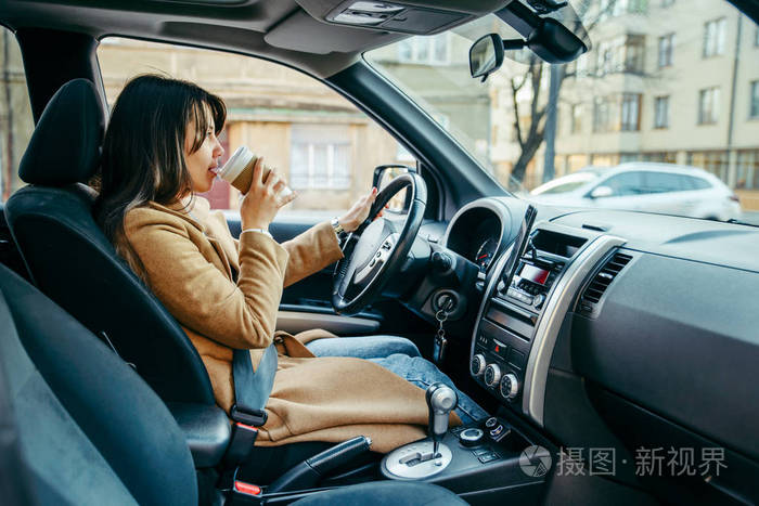 年轻漂亮的女人一边开车一边喝咖啡.生活方式
