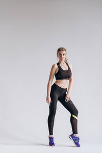 一位穿着运动服摆姿势和跳跃的年轻健身女子在灰色背景下的全身画像