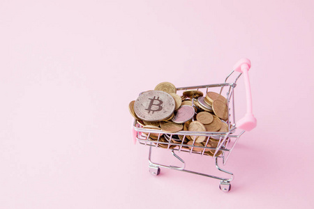 粉红色背景下购物车中的比特币和硬币。