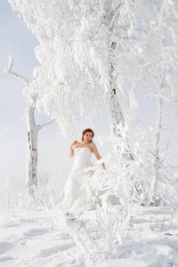 新娘穿着一件白色的裙子，背景是雪树。