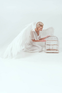 美丽的女人，穿着天使服装，翅膀摆姿势，鸟笼隔离在白色上