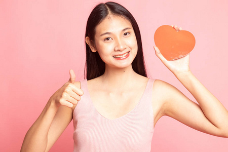 亚洲女人用红色的心在粉红色的背景上竖起大拇指