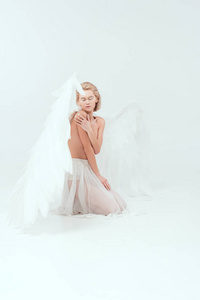 美丽的年轻女子，有着天使般的翅膀，坐着，摆出一副孤立的白色姿态