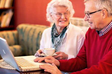 老太太端着一杯茶，而她的伴侣看着他的笔记本电脑