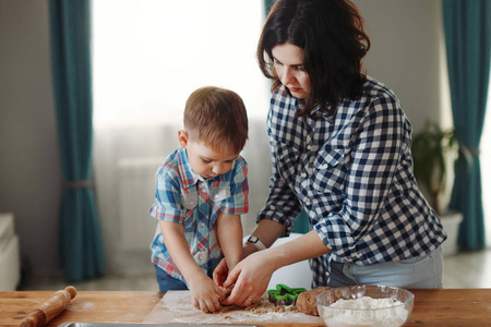 母亲和儿子穿着格子衬衫，在厨房里煮面粉和面团