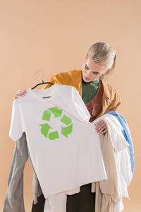 年轻女性看着生态服装，衣架上有回收标志，隔离在米色环保概念上